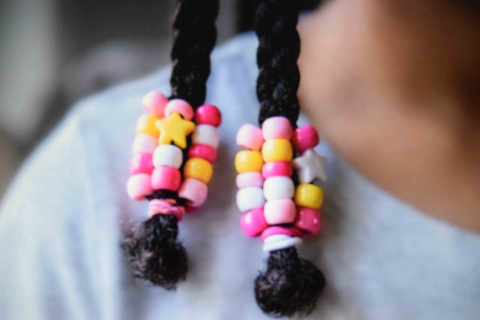 Pink and yellow plastic beads threaded onto the ends of two small braids