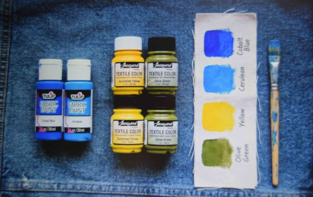 Fabric paint bottles and test swatches laid out on denim before starting a pocket design