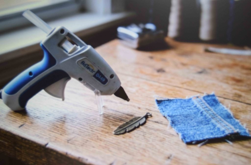 A low temperature glue gun set up beside denim and a charm on a flat work board