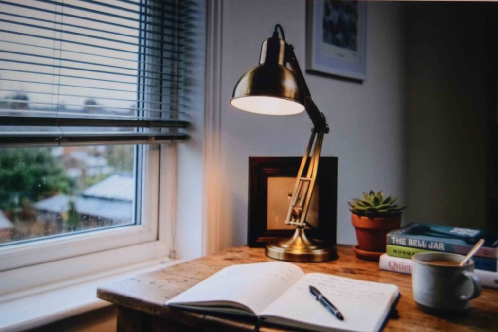 A desk lamp and lowered blinds handling glare and gray daylight in a learning space
