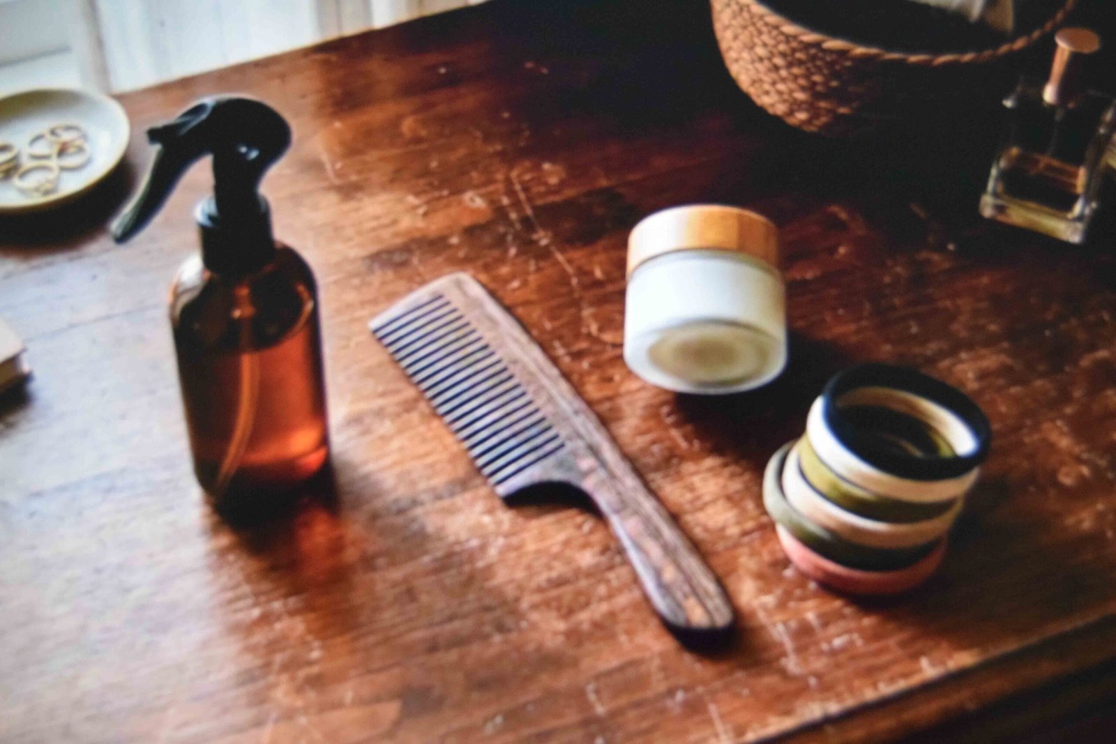 Comb, spray bottle, elastics and leave-in cream laid out on a bedroom dresser