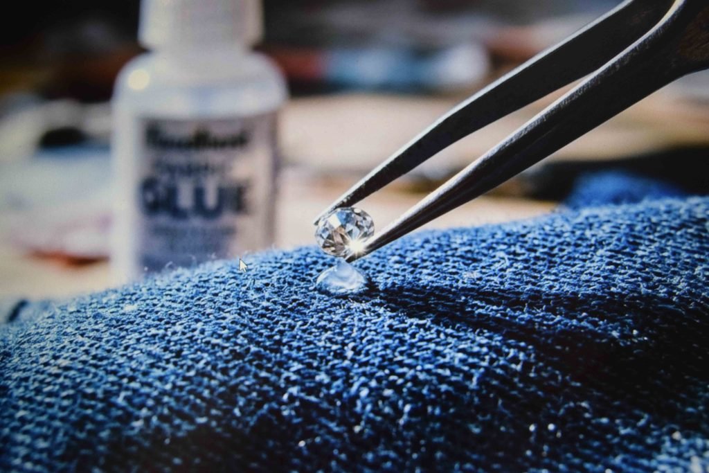 A rhinestone being pressed into place on a denim pocket with fabric glue