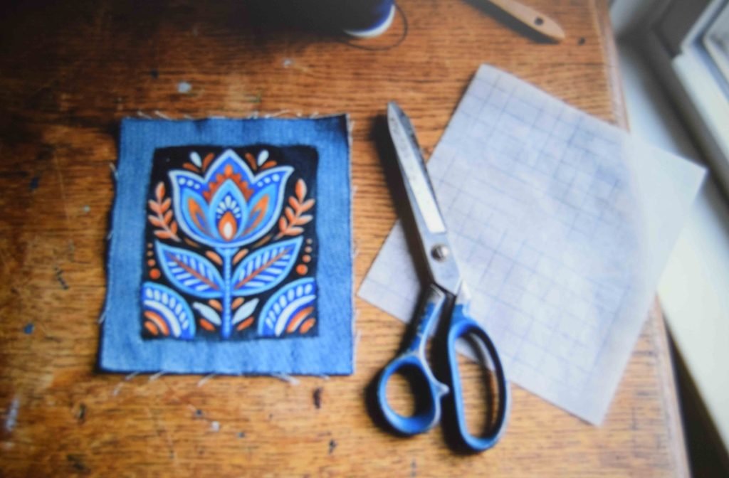 A painted denim scrap being prepared as an iron on patch for a jean pocket