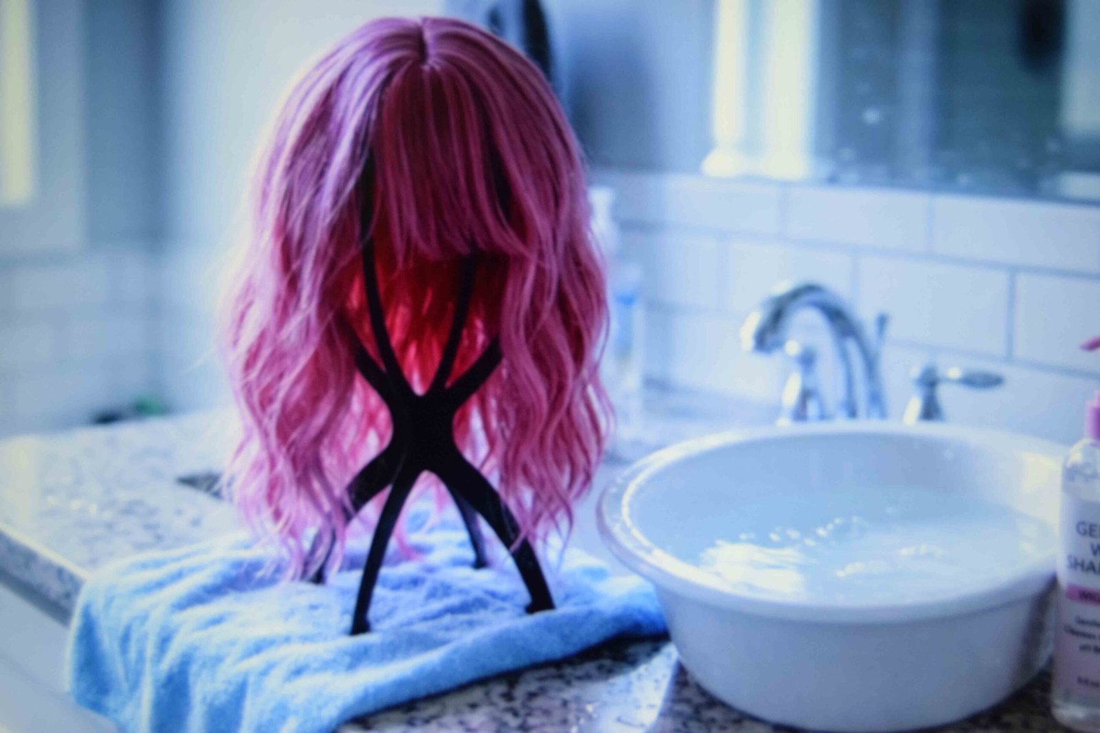 A pink wig air drying on a stand after a cool water wash