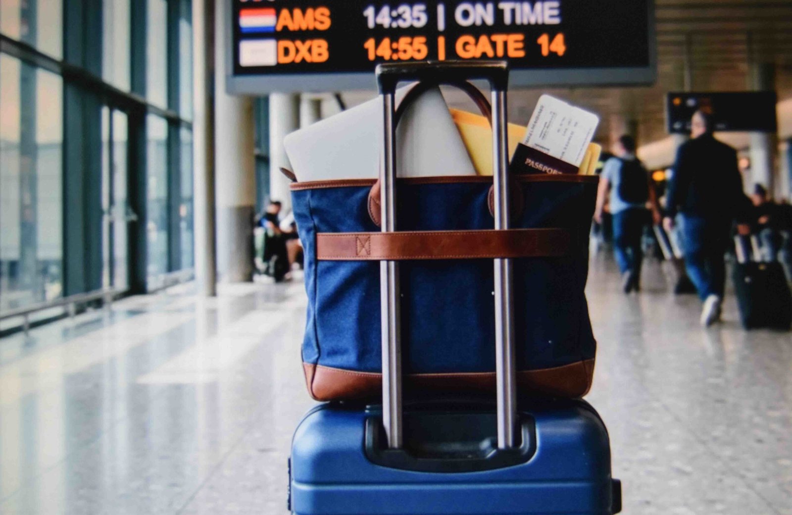 A structured tote sitting on a carry on handle for hands free airport travel