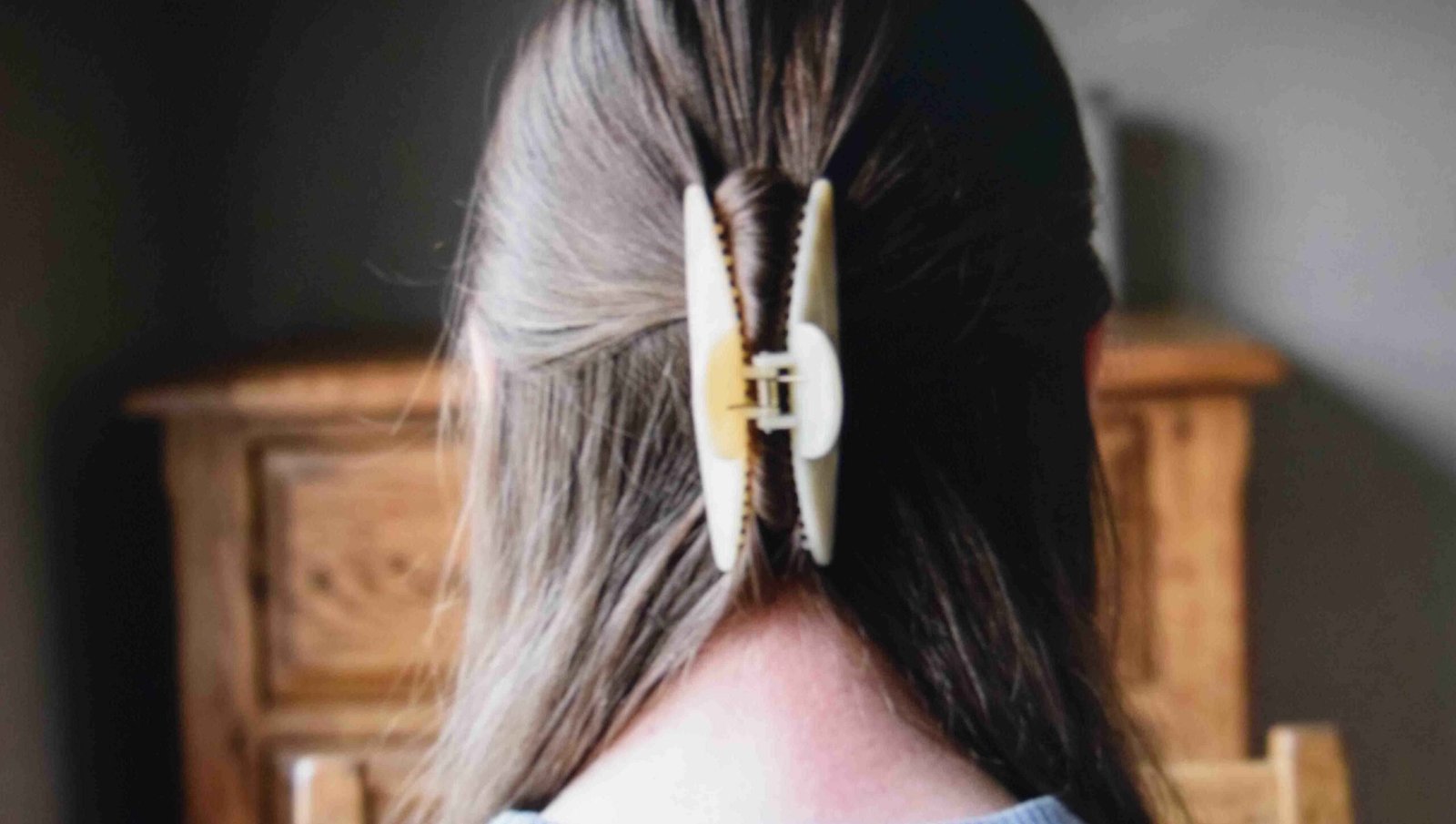 Narrow claw clip holding a twisted half up section in silky fine hair seen from behind