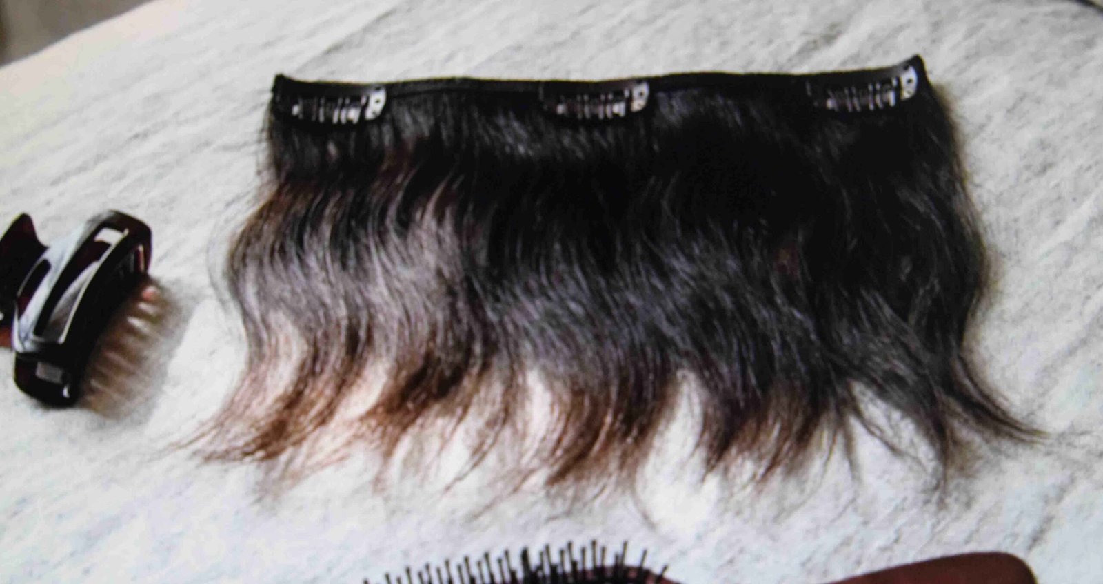 Hair extension weft with three track clips laid beside a claw clip on a linen bedspread