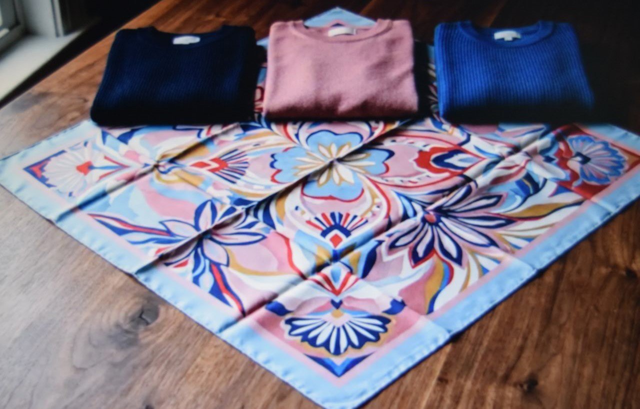 Multicolour printed scarf laid beside three knit tops matching separate shades in the print