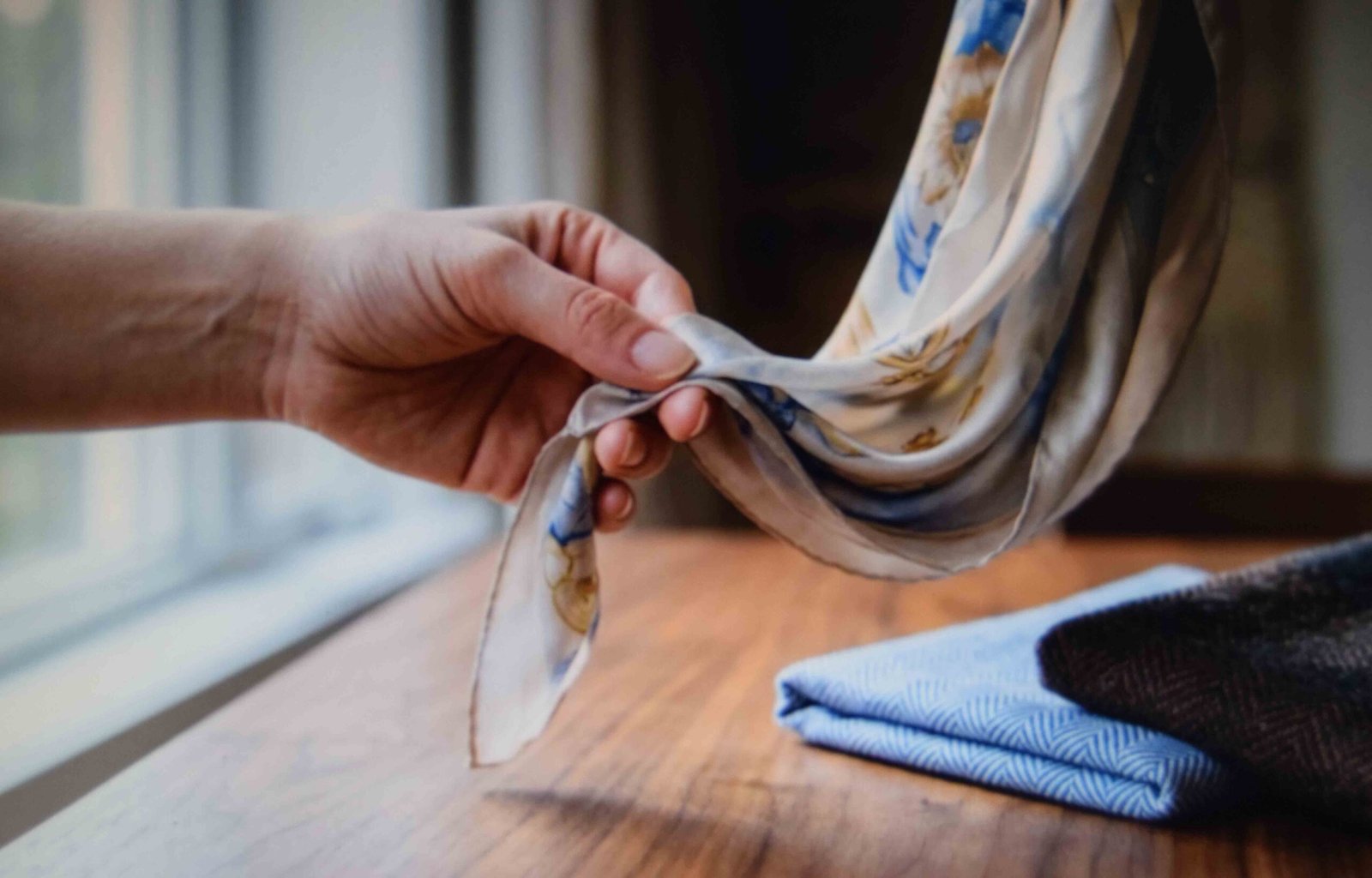Hand holding a silk scarf by one corner to show how the fabric drapes before tying