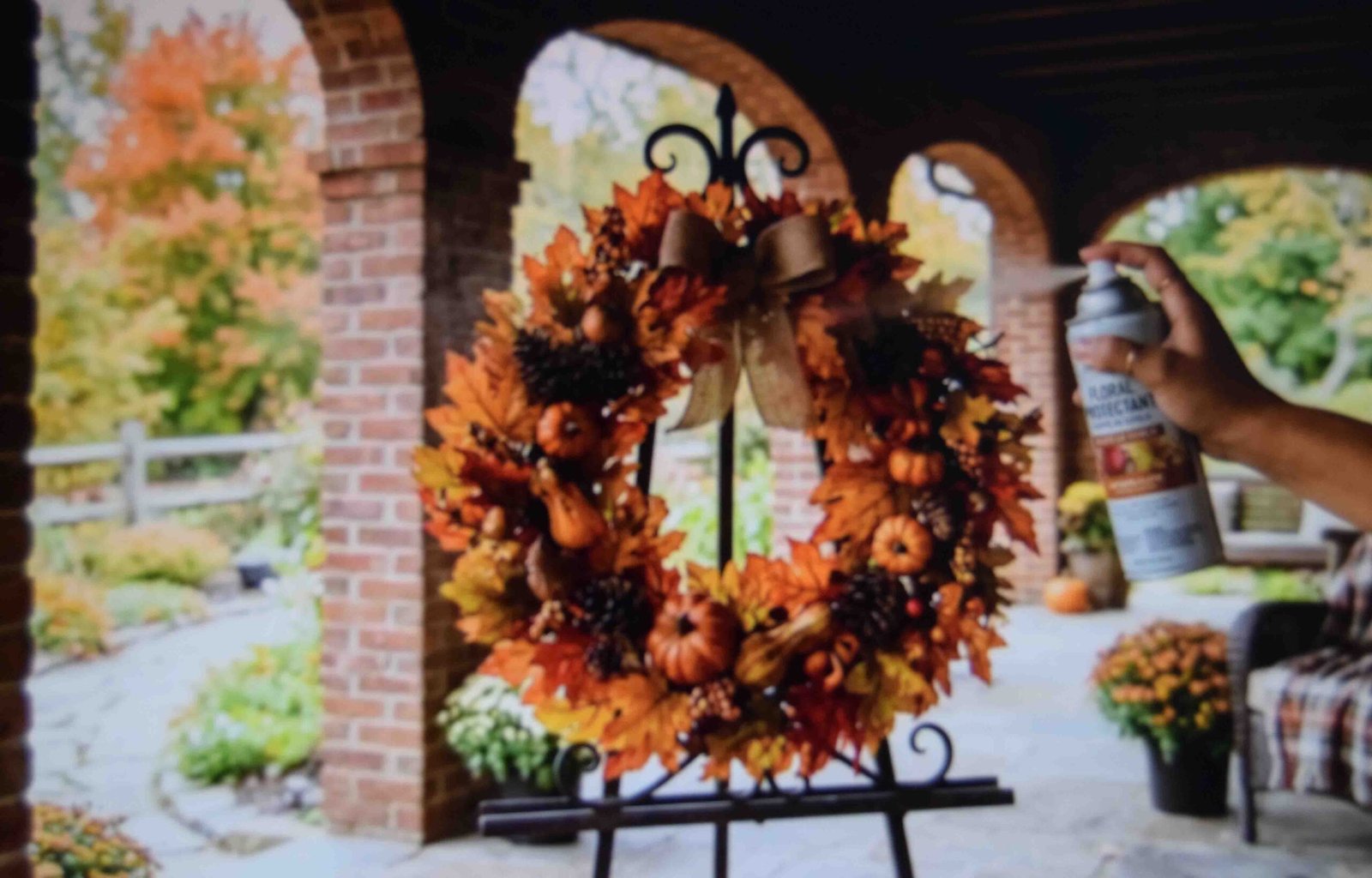 Finished autumn wreath on an outdoor easel being misted with clear UV protective sealant spray.