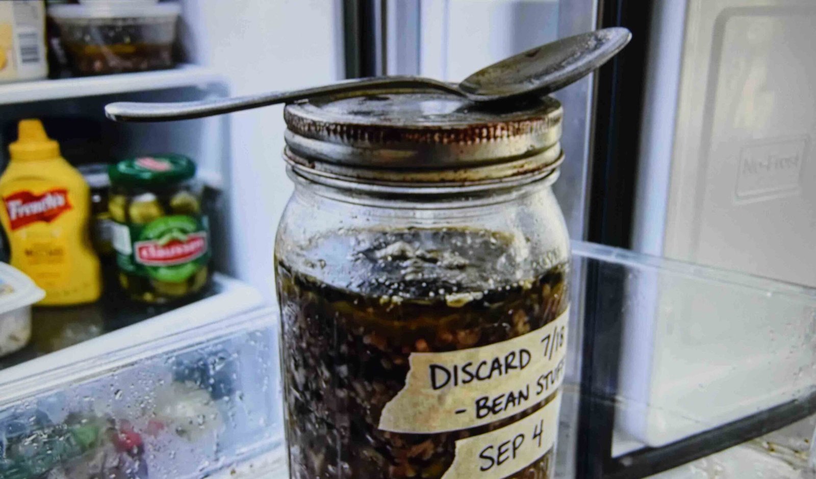 A collection jar of discard stored in the fridge with liquid separating on top