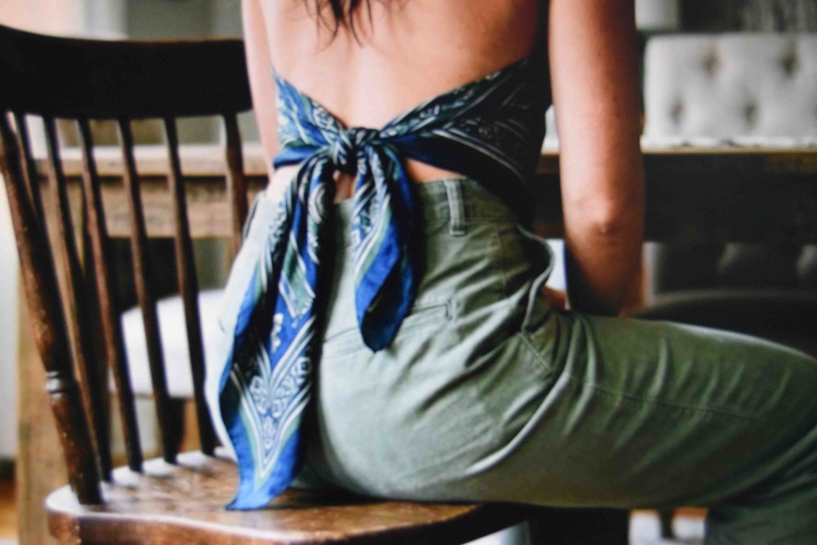 Scarf knotted at the small of the back with equal tails falling over trousers while seated