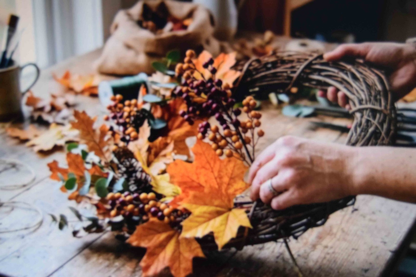 Deep red berry branches being woven between the branches of an autumn wreath to add color contrast.